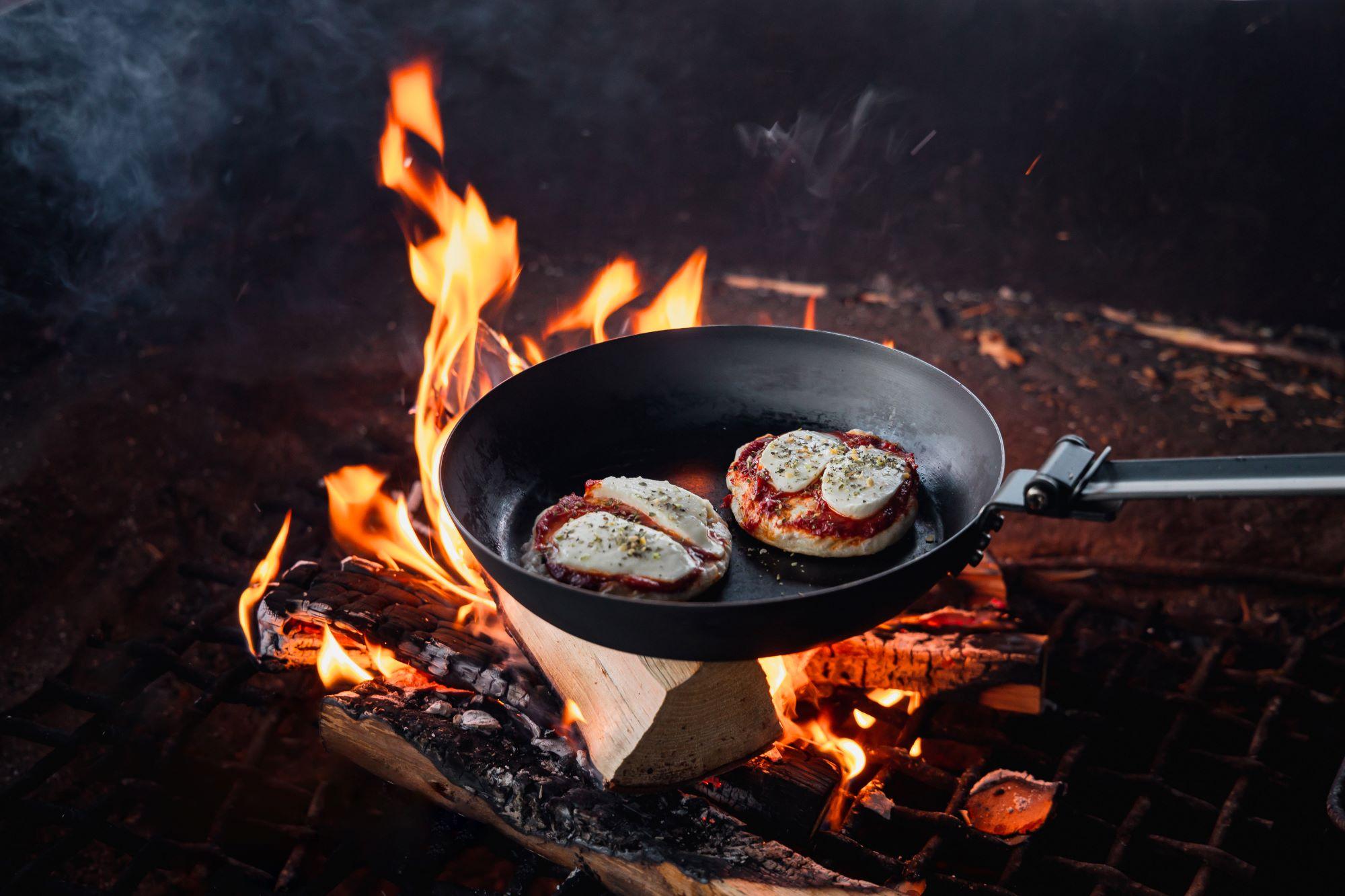 Paistinpannu nuotiolla. Paistinpannussa on kaksi pientä mozzarellapitsaa.